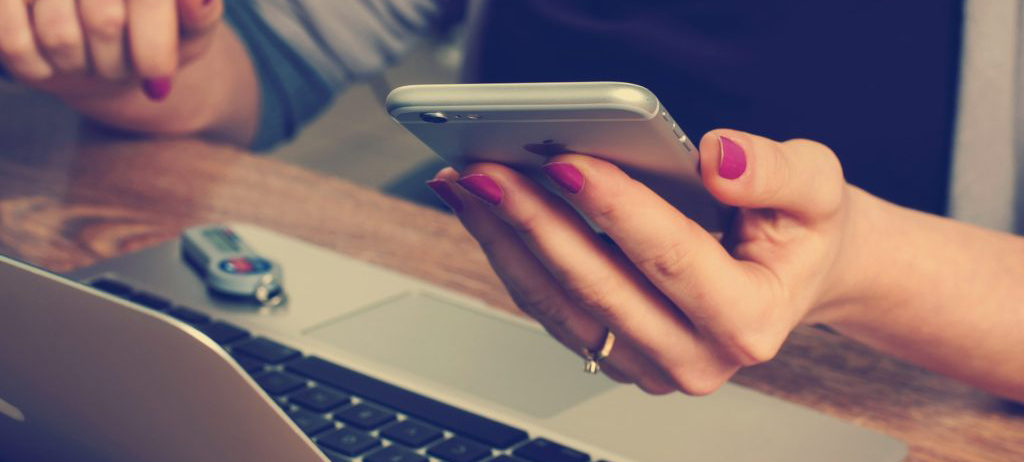 detail of woman's hands using a laptop and holding a smartphone